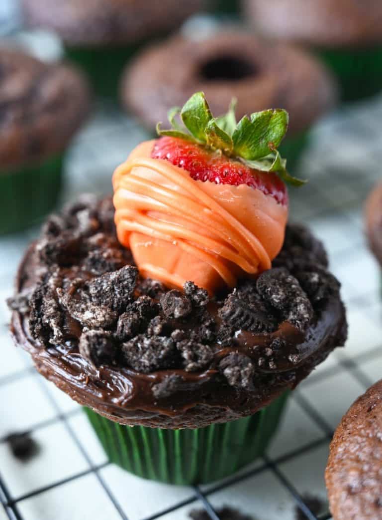 Chocolate dipped strawberry that looks like a carrot on top of a chocolate frosted cupcake with oreo crumbles on top to look like dirt.