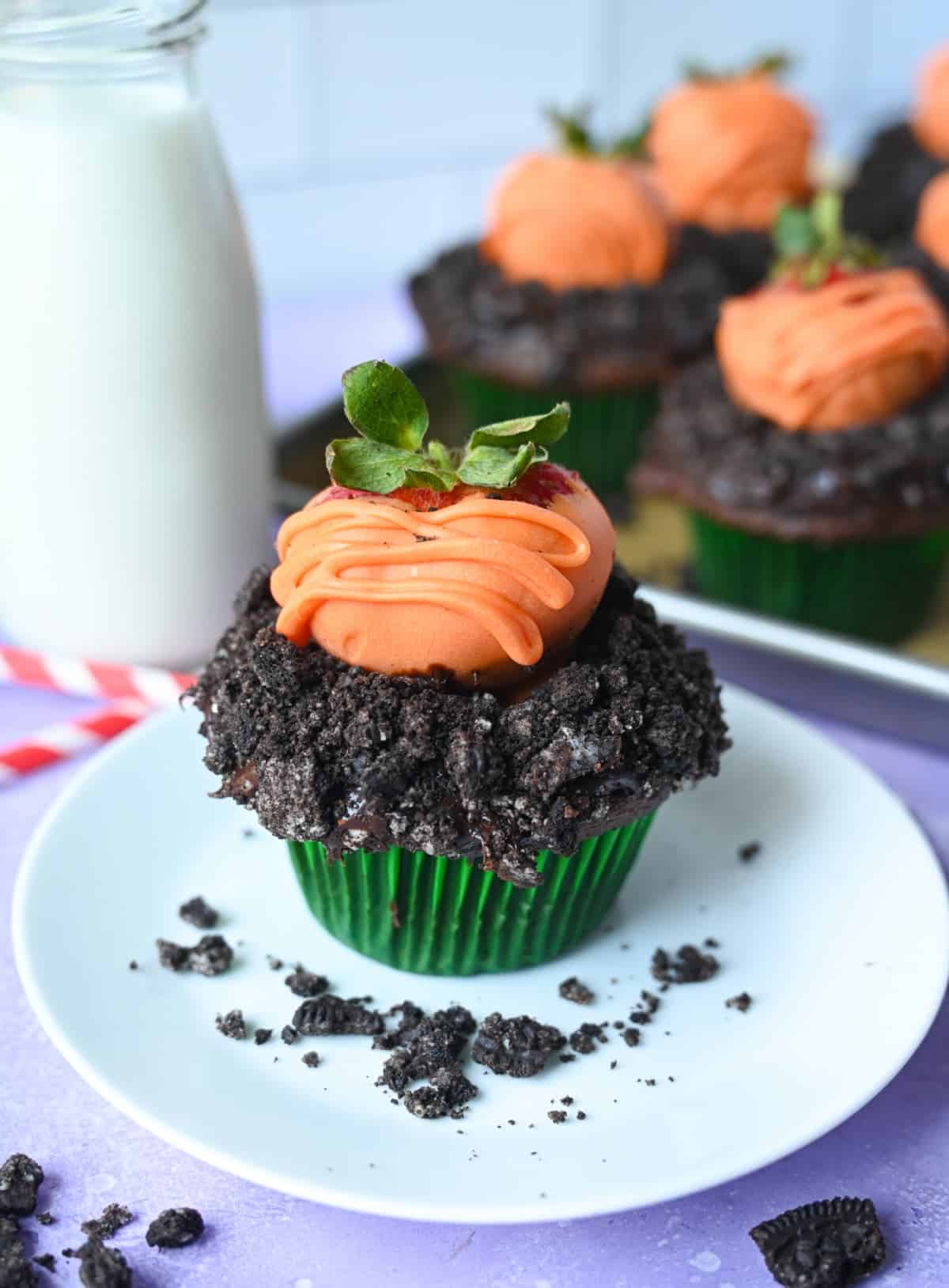 One chocolate cupcake with oreo crumbs on top and a chocolate covered strawberry on top to look like a carrot.