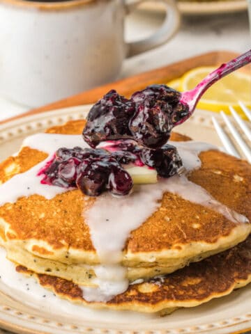 A stack of poppyseed pancakes with blueberry compote on top.