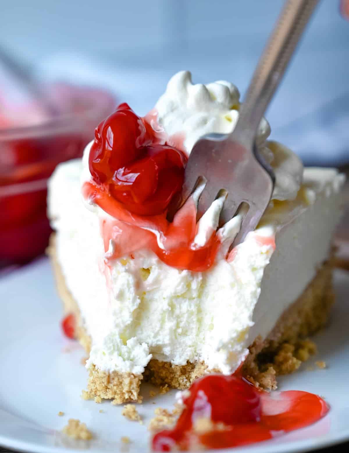A close up photo of a fork cutting into a piece of cheesecake.