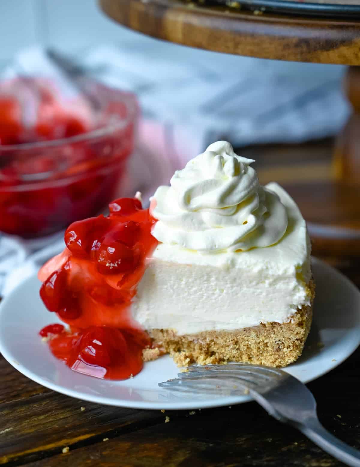 A slice of cheesecake on a small white plate with whipped cream and cherries on top.