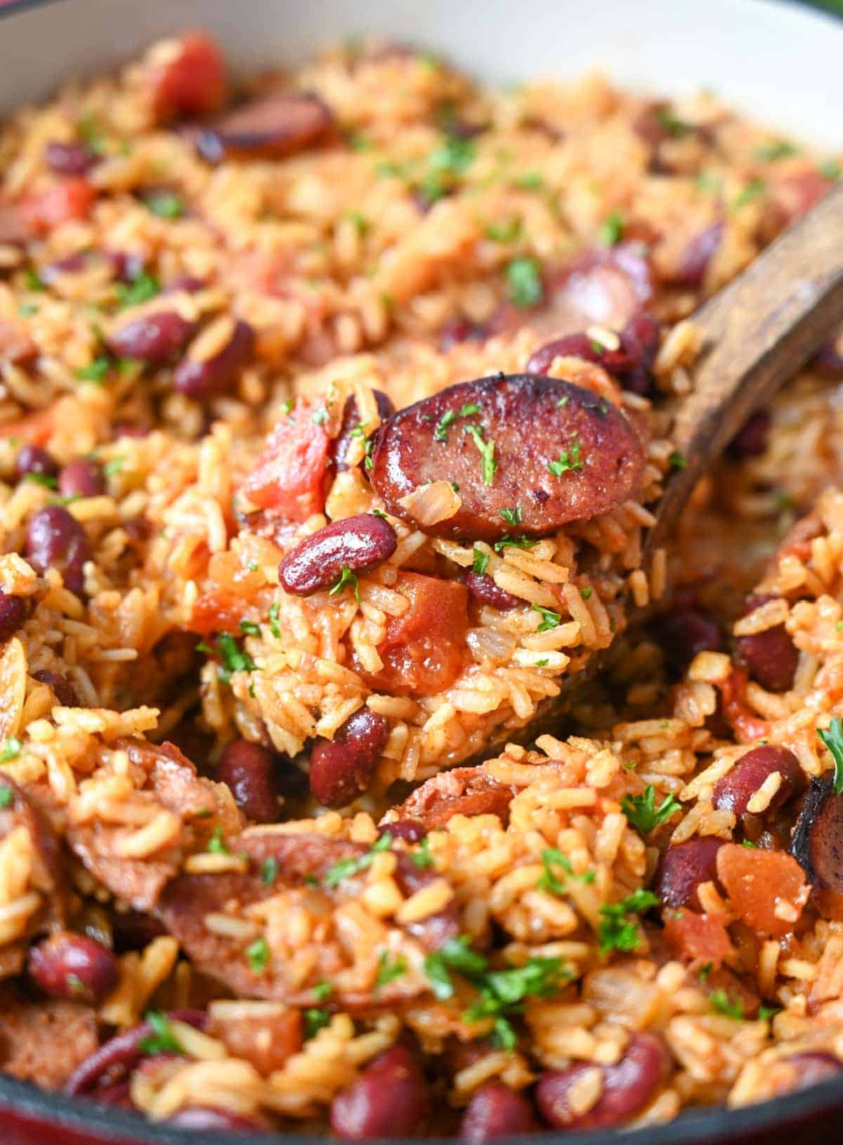 Cajun rice and beans in a skillet with a wooden spoon scooping some out.