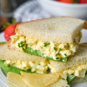 Small cut egg salad sandwiches stacked on top of each other.
