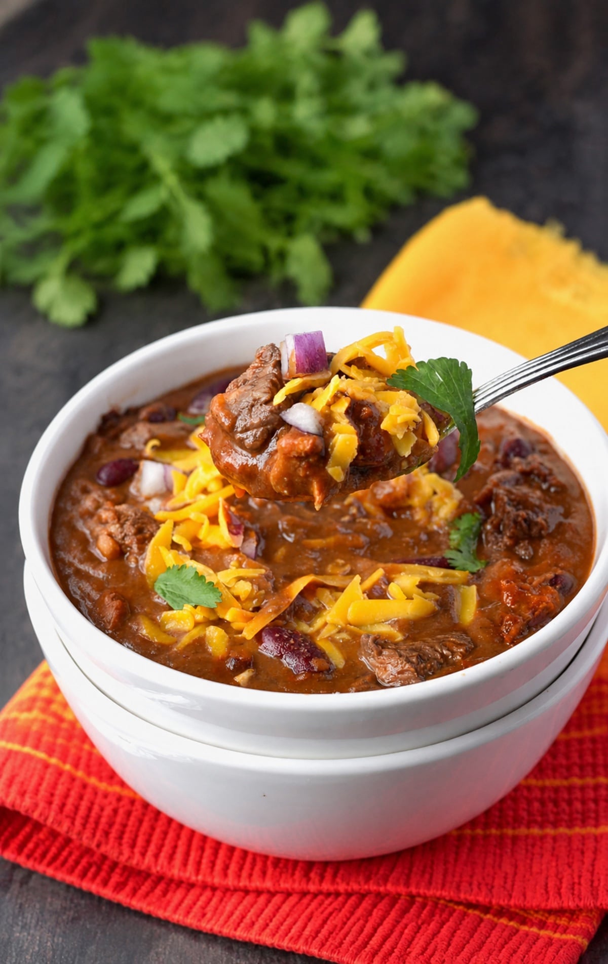 A bowl of steak chili with a spoon taking a bite out of it.