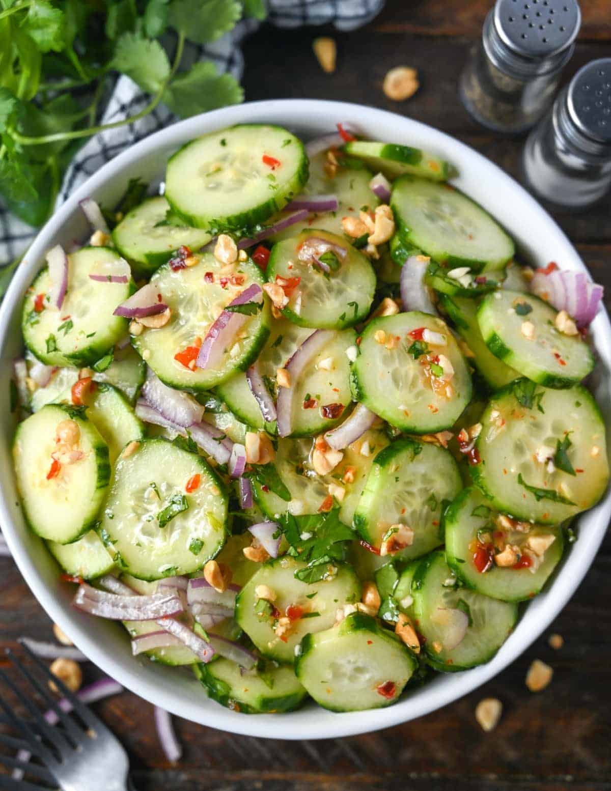 A big white bowl of cucumber salad with red onions and peanuts on top.