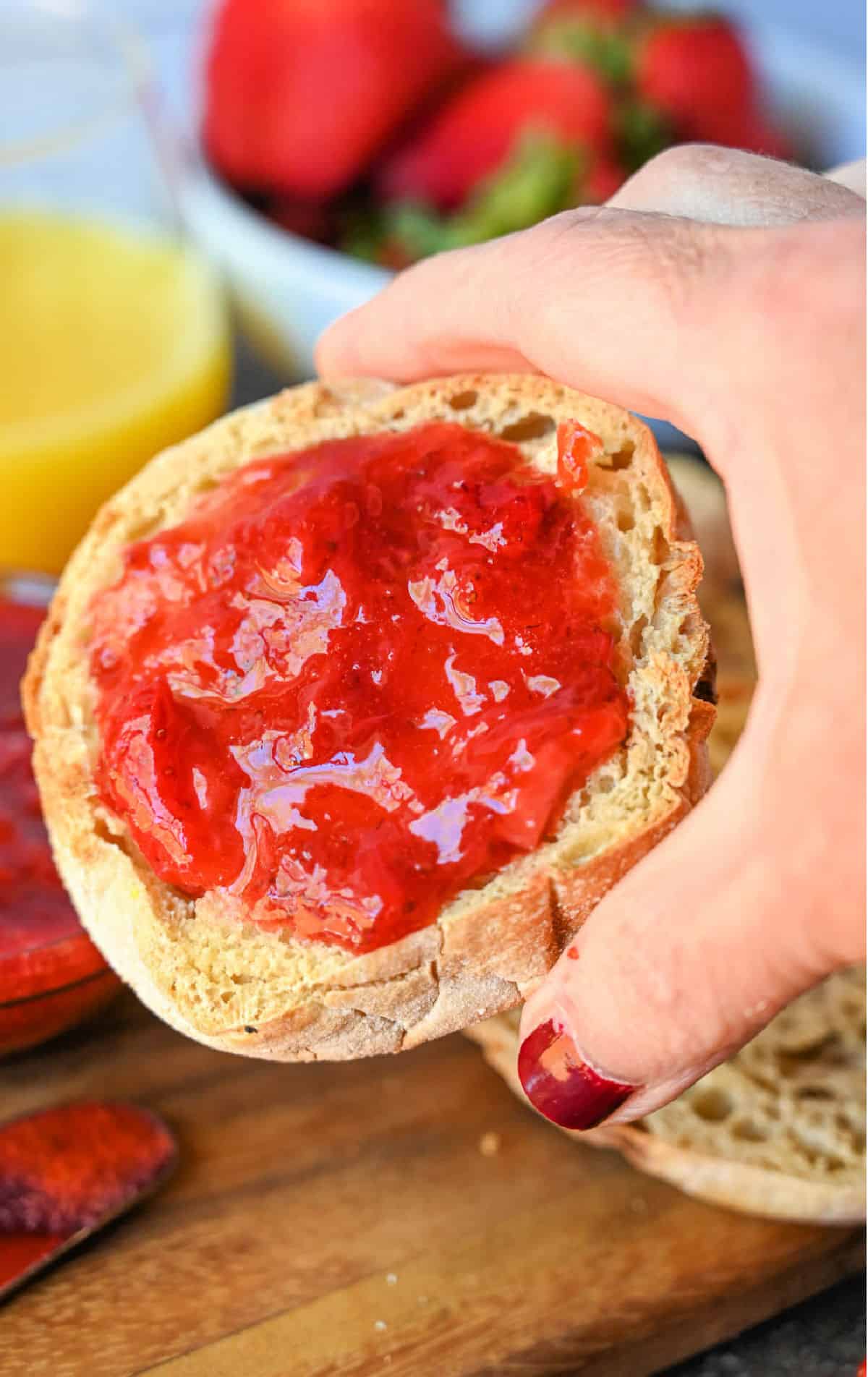 Holding an english muffin with strawberry jam.