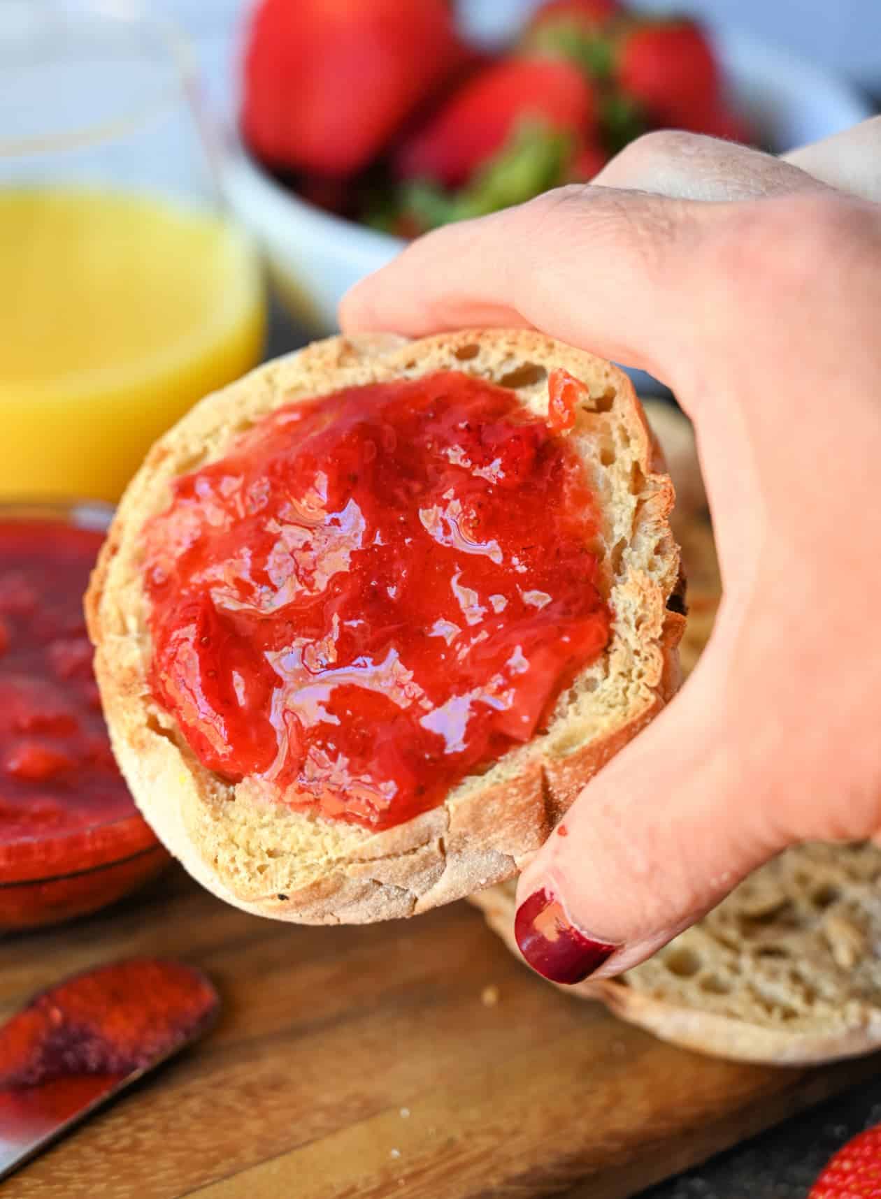 Strawberry jam spread on an english muffine and being held.