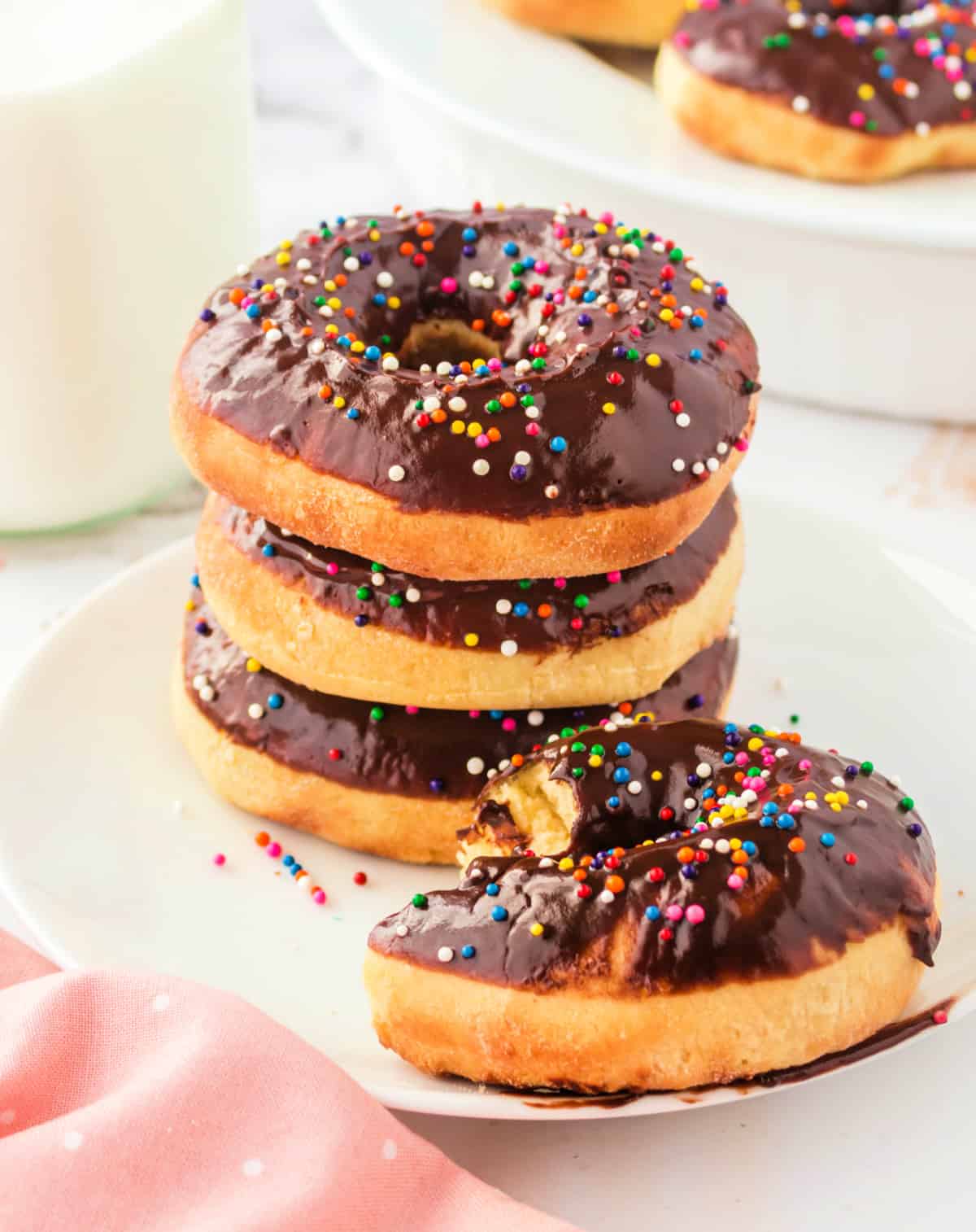 A stack of air fried donuts with chocolate frosting and one with a bite out of it.