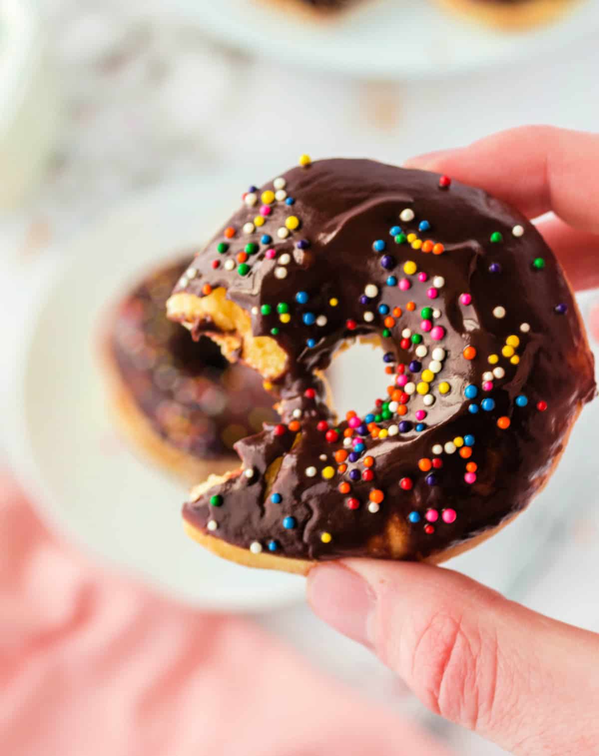 A air fryer chocolate dipped donuts being held with a bite out of it.