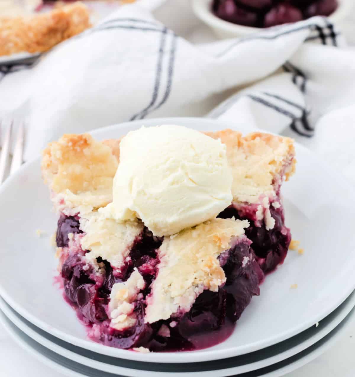 A clice of cherry pie on a white plate.