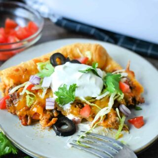 A serving of taco crescent roll bake on a white plate with tomatoes, olives lettuce and sour cream.