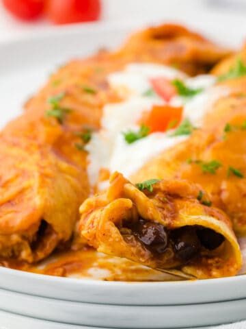 Two beef enchiladas on a white plate with cour cream a fork.