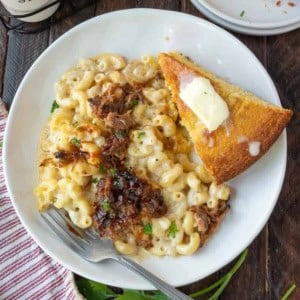 Pulled pork mac and cheese on a white plate with a side of cornbread.