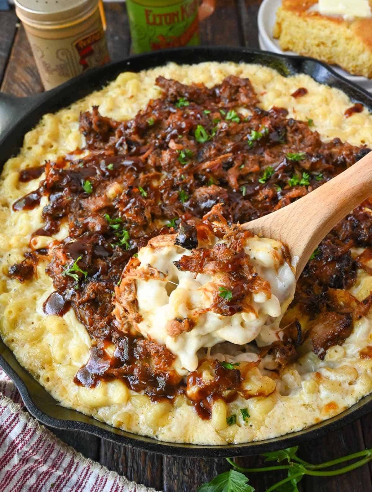 Pulled pork mac and cheese in a cast iron skillet with a wooden spoon scooping some out.