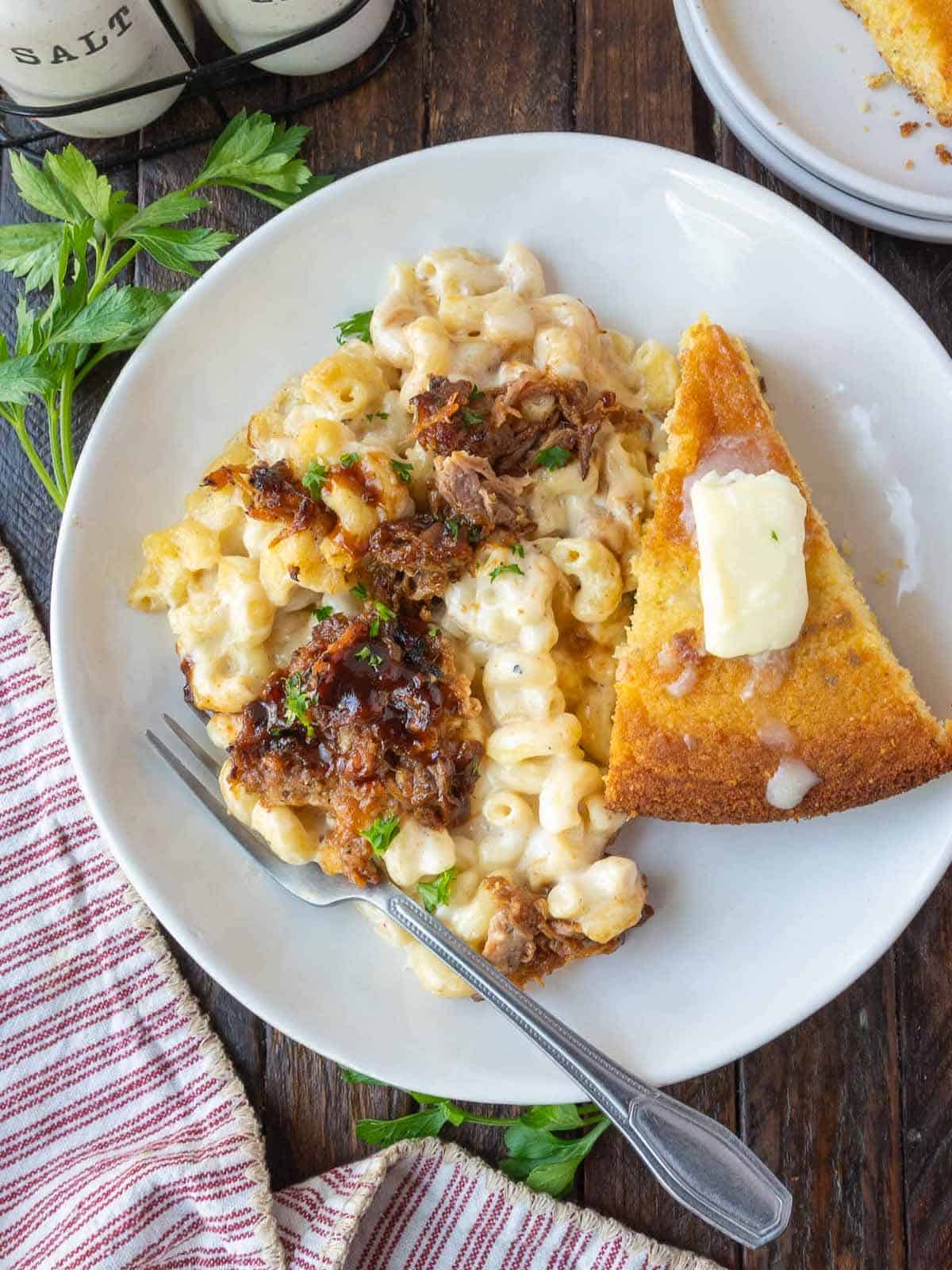 Pulled pork mac and cheese on a white plate with a side of cornbread.