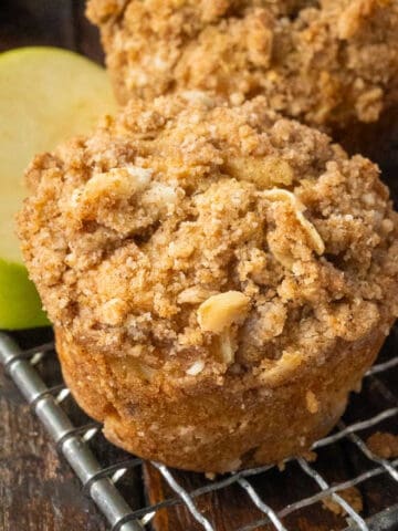 Apple muffin on a cooling rack with slices of apples.