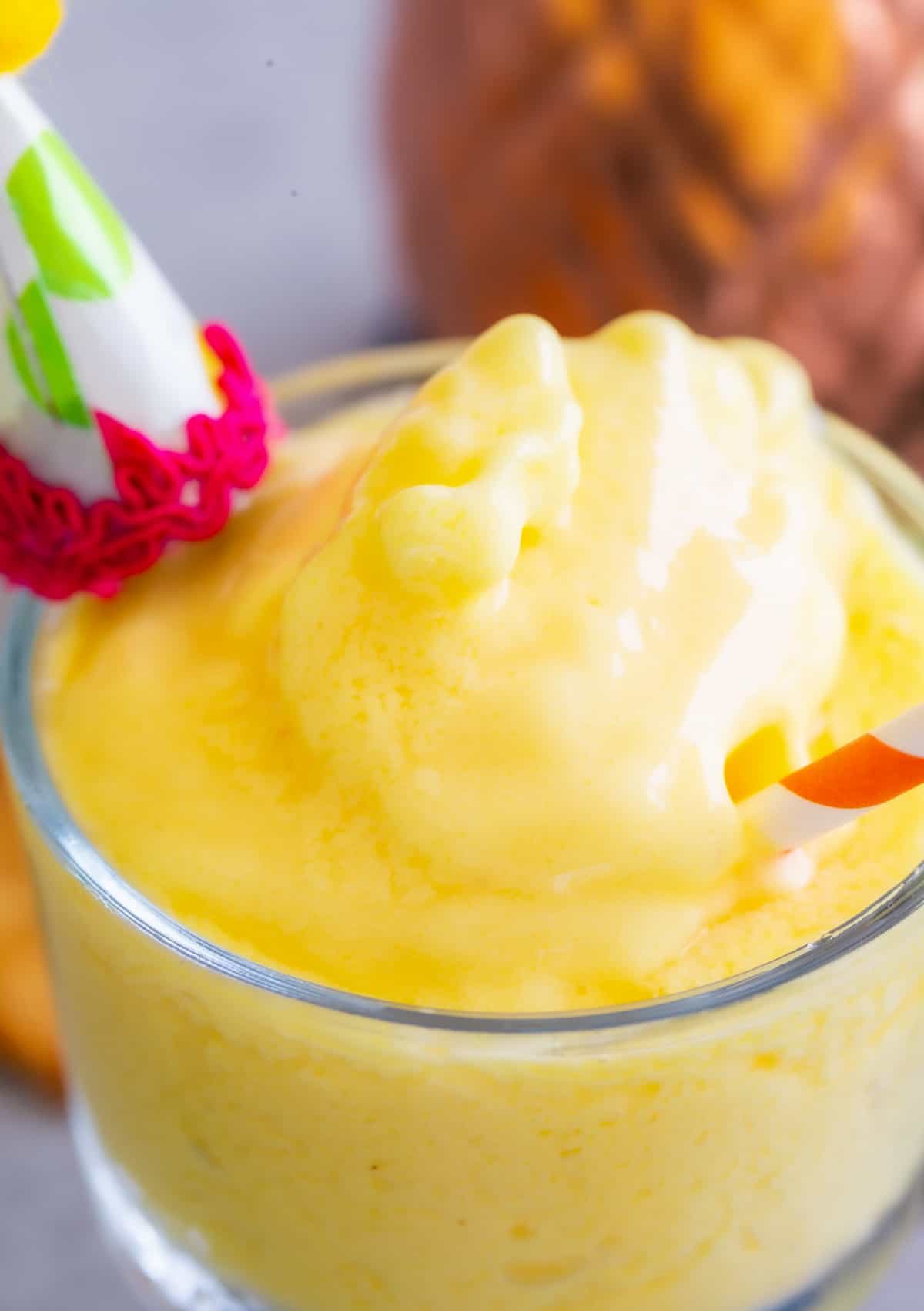 Close up photo of pineapple dole whip in a glass with a red striped straw.