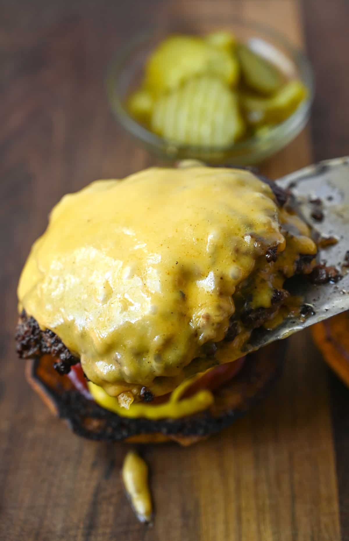Spatula placing a double layed burger with chees on top of a bun.