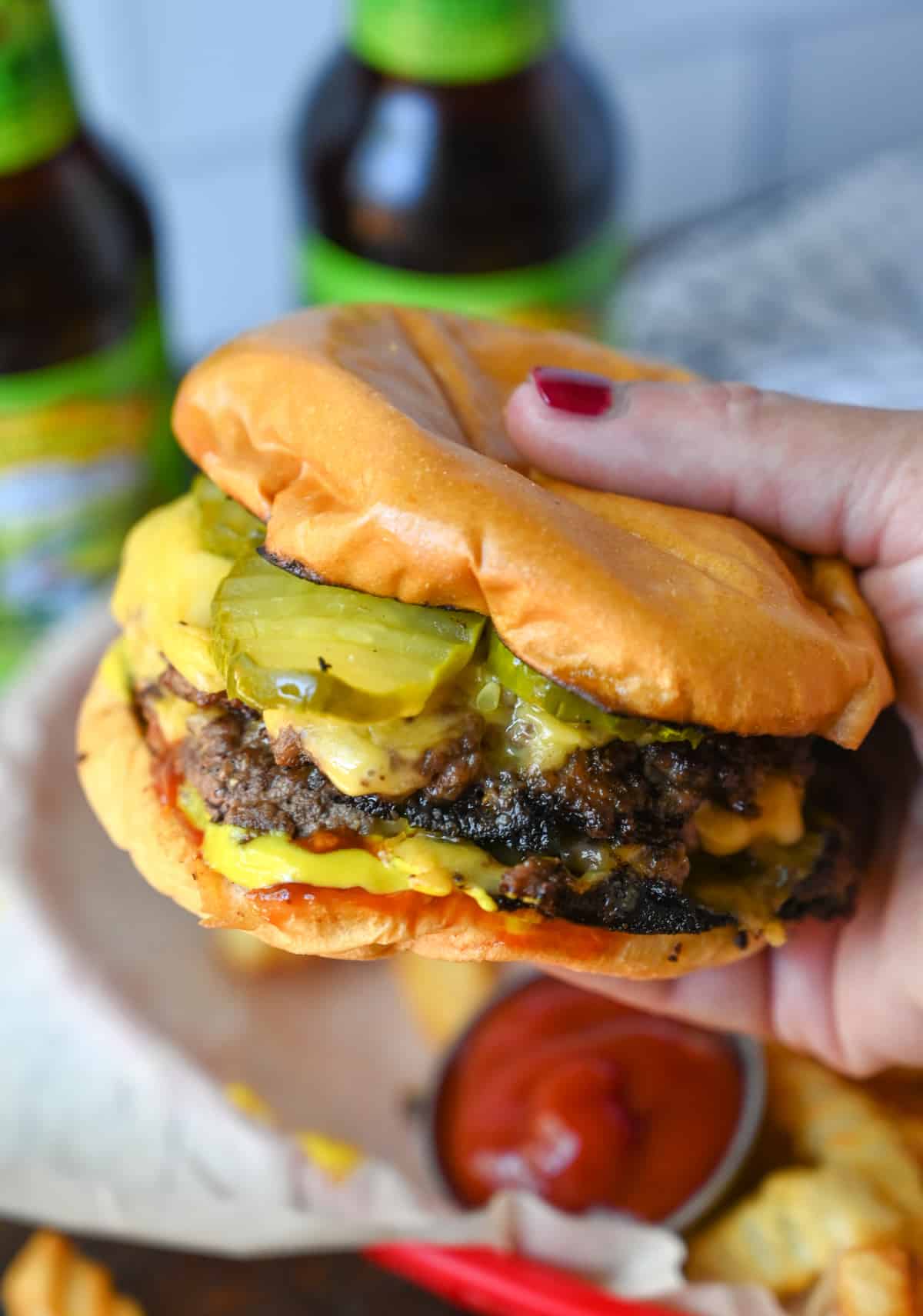Smash burger with cheese and pickles being held in a hand.