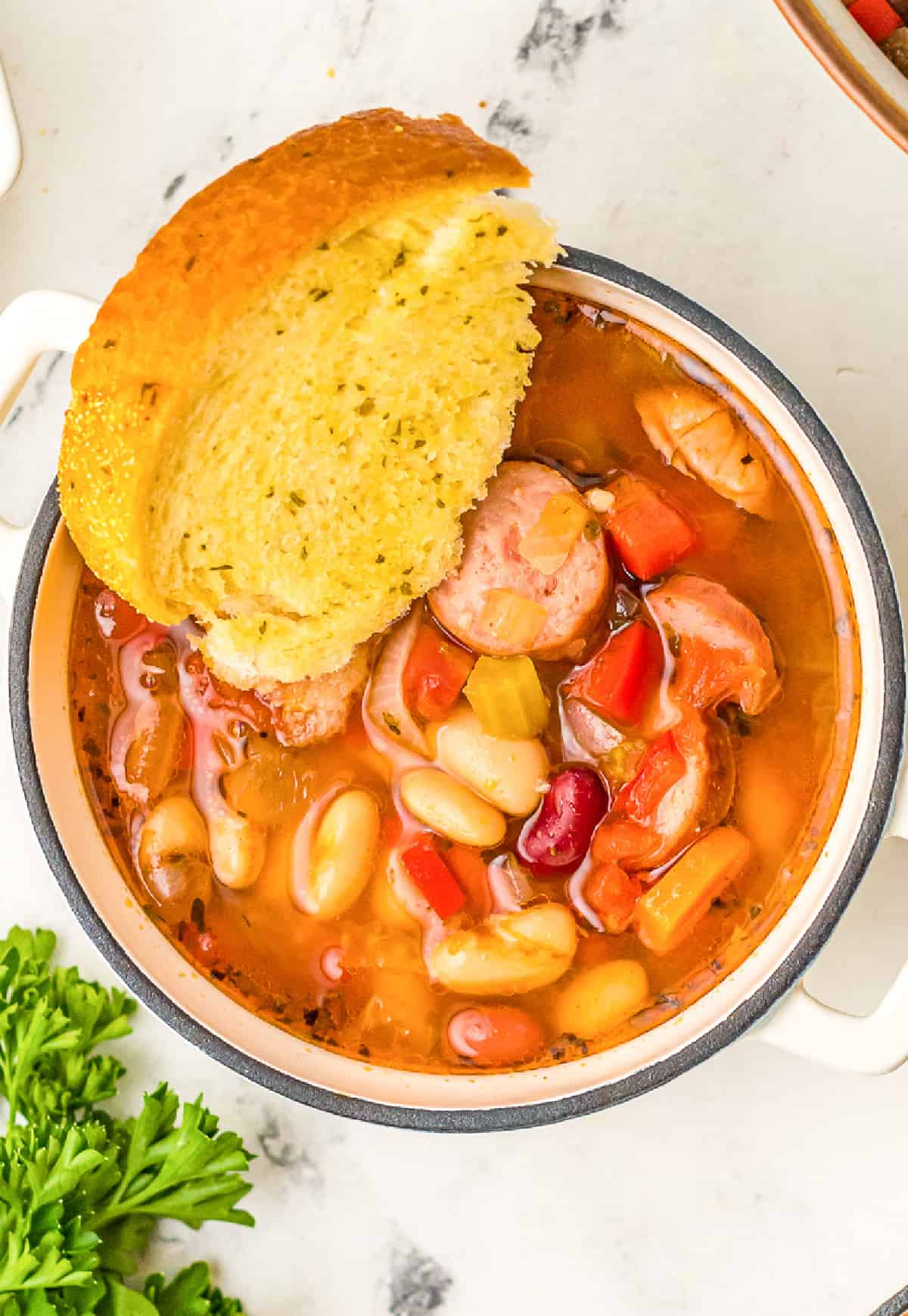 a small bowl of sausage bean soup with a slice of garlic bread.