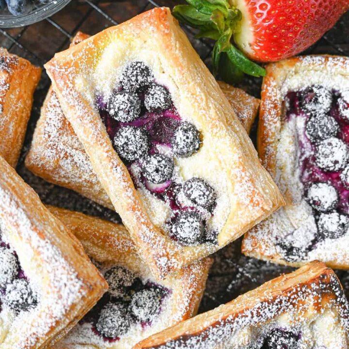 A pile of blueberry cream cheese pastries with a side of strawberries.