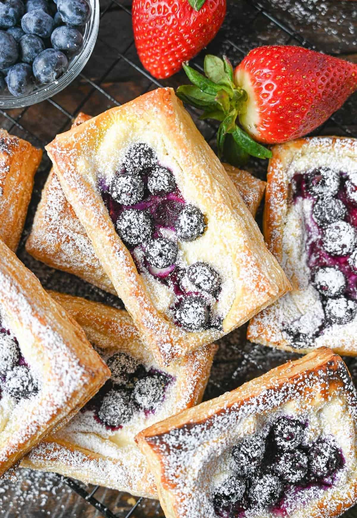 A pile of blueberry cream cheese pastries with a side of strawberries.