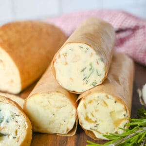 Three rolled herb compound butters in parchment paper.