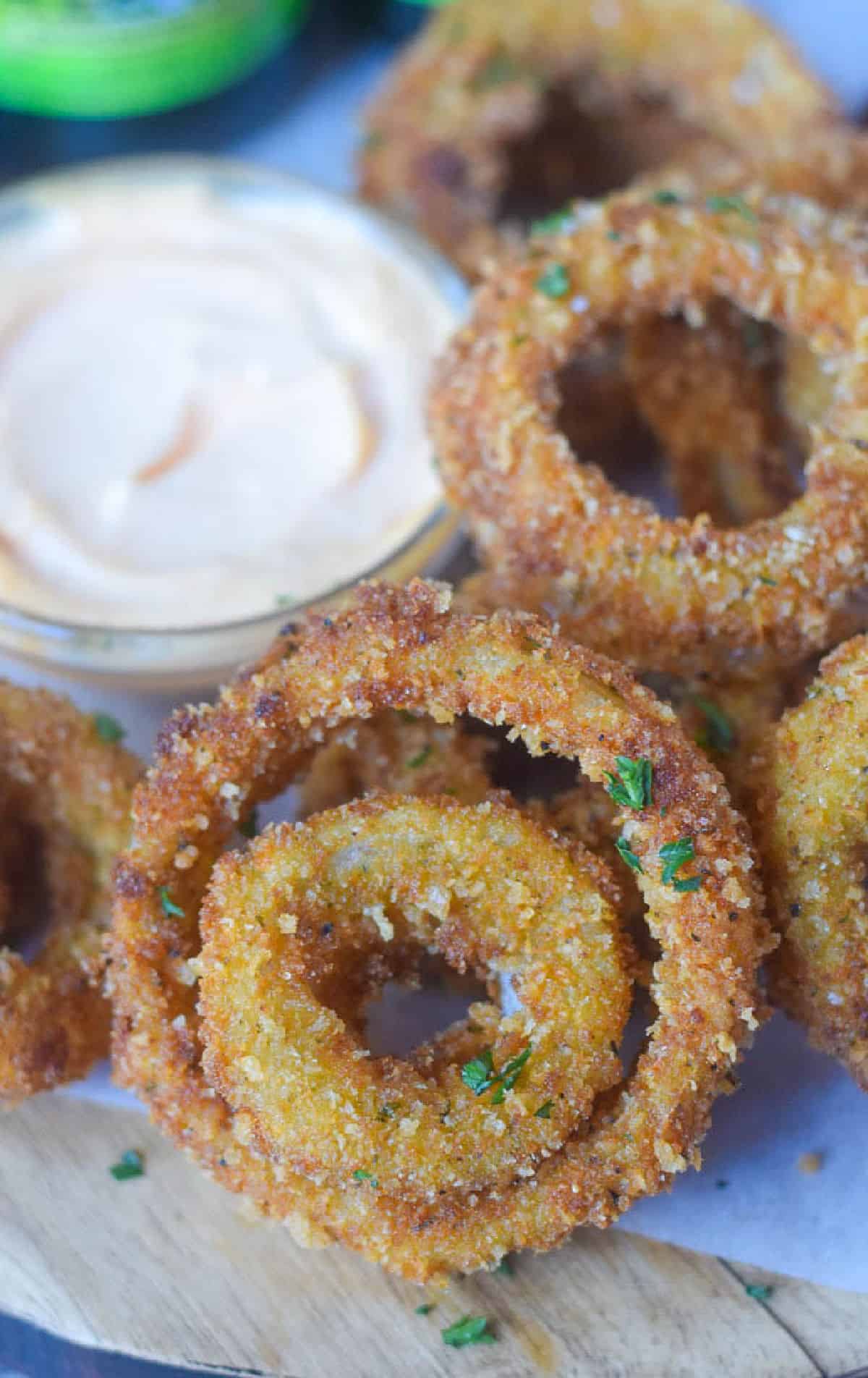 a few onion rings piled on top of each other and a side of sriracha sauce.