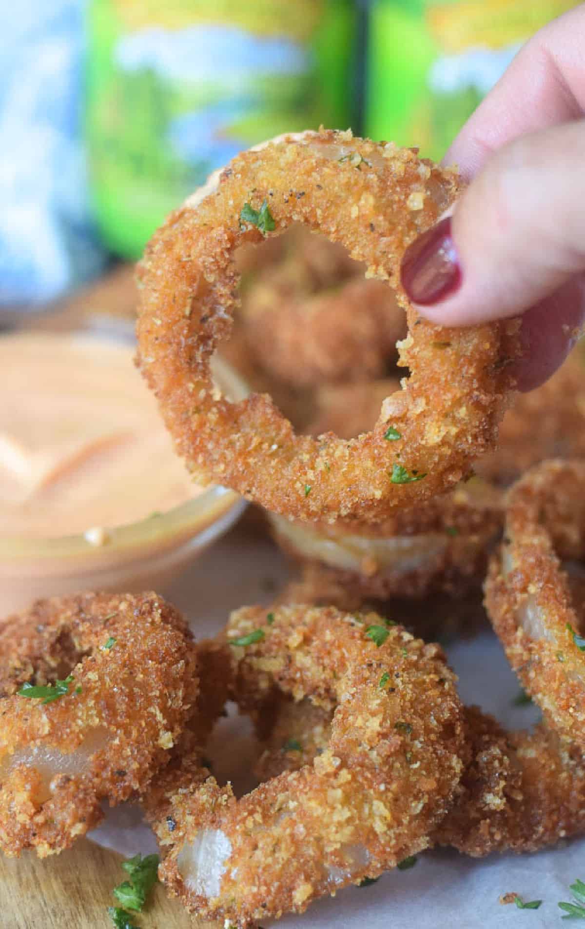 A parmesan onion ring being picked up and ready to eat.