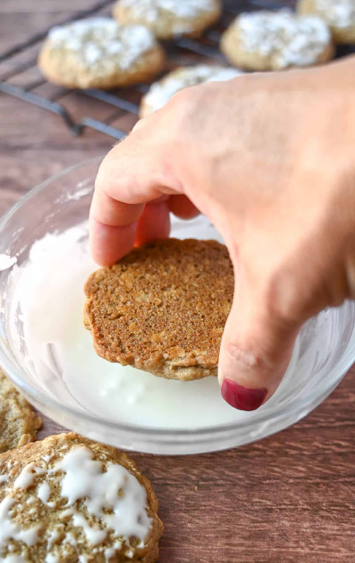 An oatmeal cookie being dipped into icing.