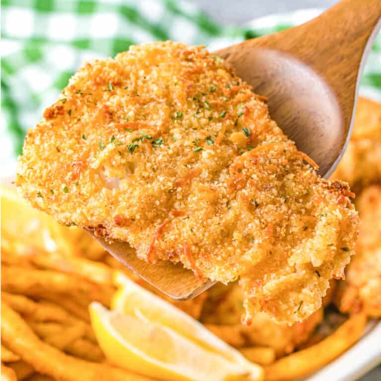 A close up photo of a wooden spatula picking up a breaded fish filet.