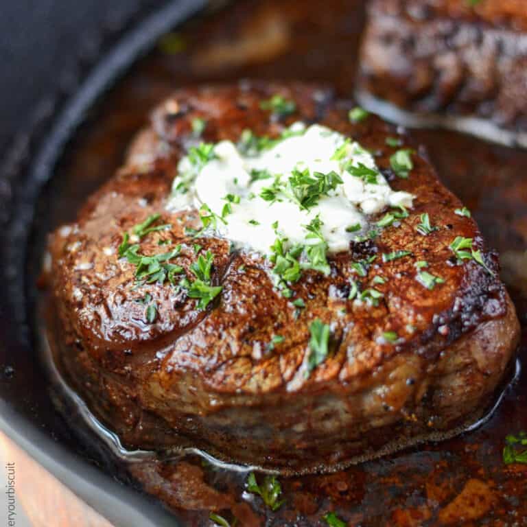 A close up photo of filet mignon steak in a cast iron pan with a dab of garlic herb butter.