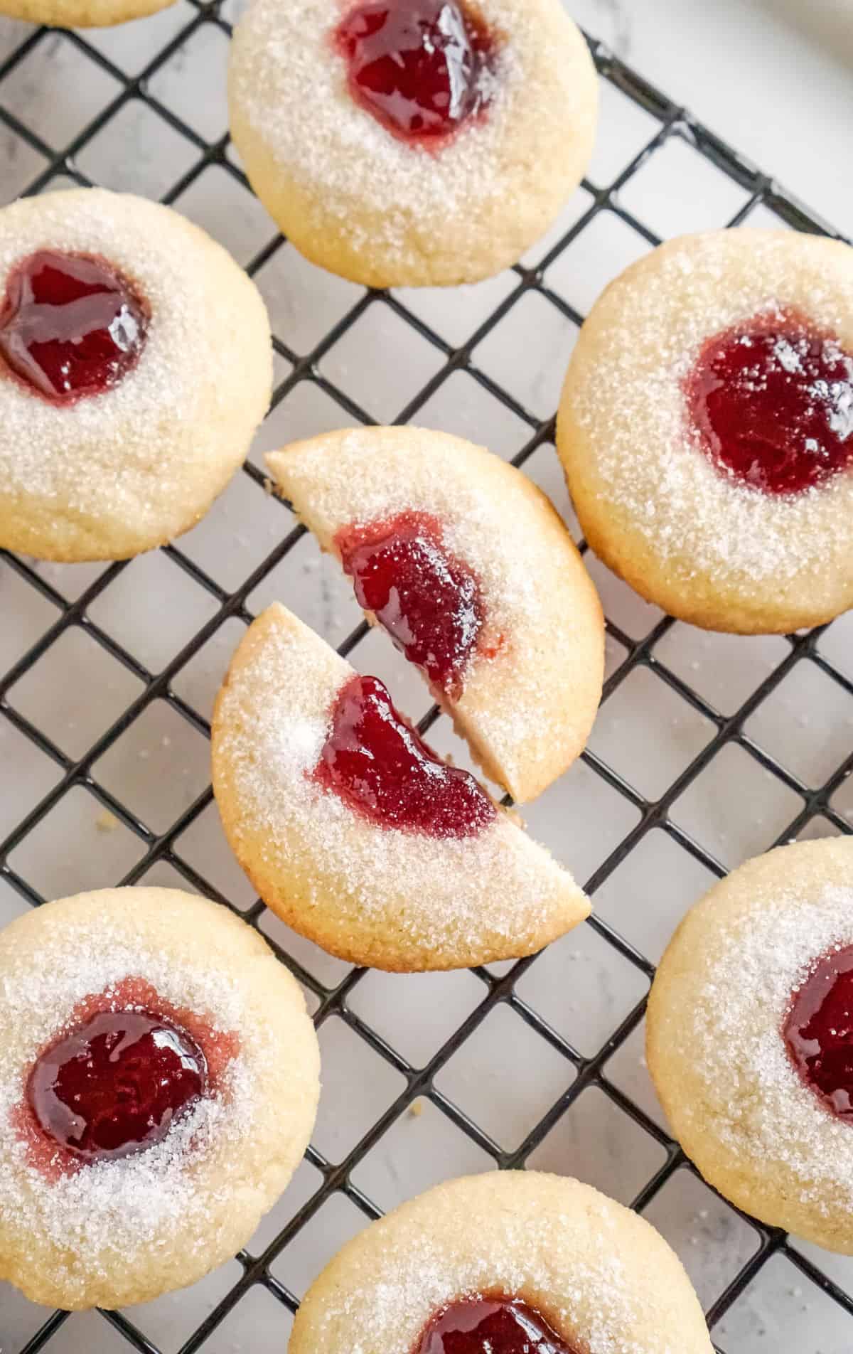 Several raspberry thumbprint cookies on a cooling rack. One has been cut in half.