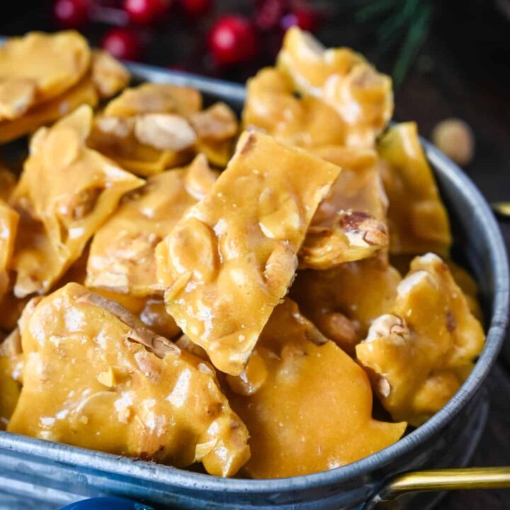 Microwave peanut brittle in a metal tin with some Christmas ornaments laying on the side.