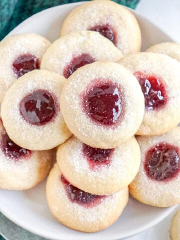 Several raspberry thumbprint cookies on a white plate.