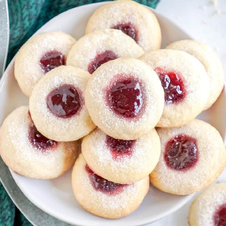 Several raspberry thumbprint cookies on a white plate.