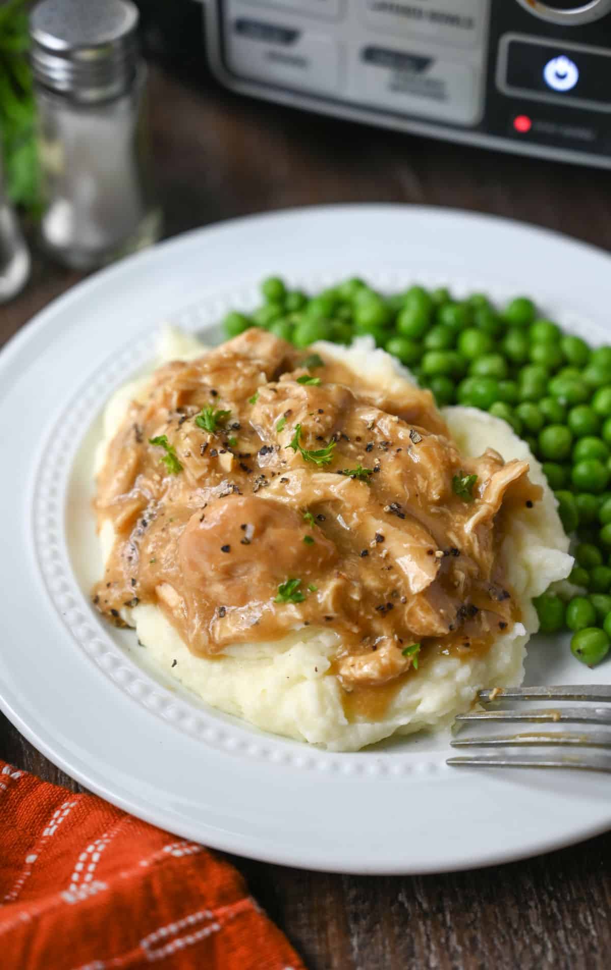 Slow cooker chicken and gravy on mashed potatoes and a side of green peas.