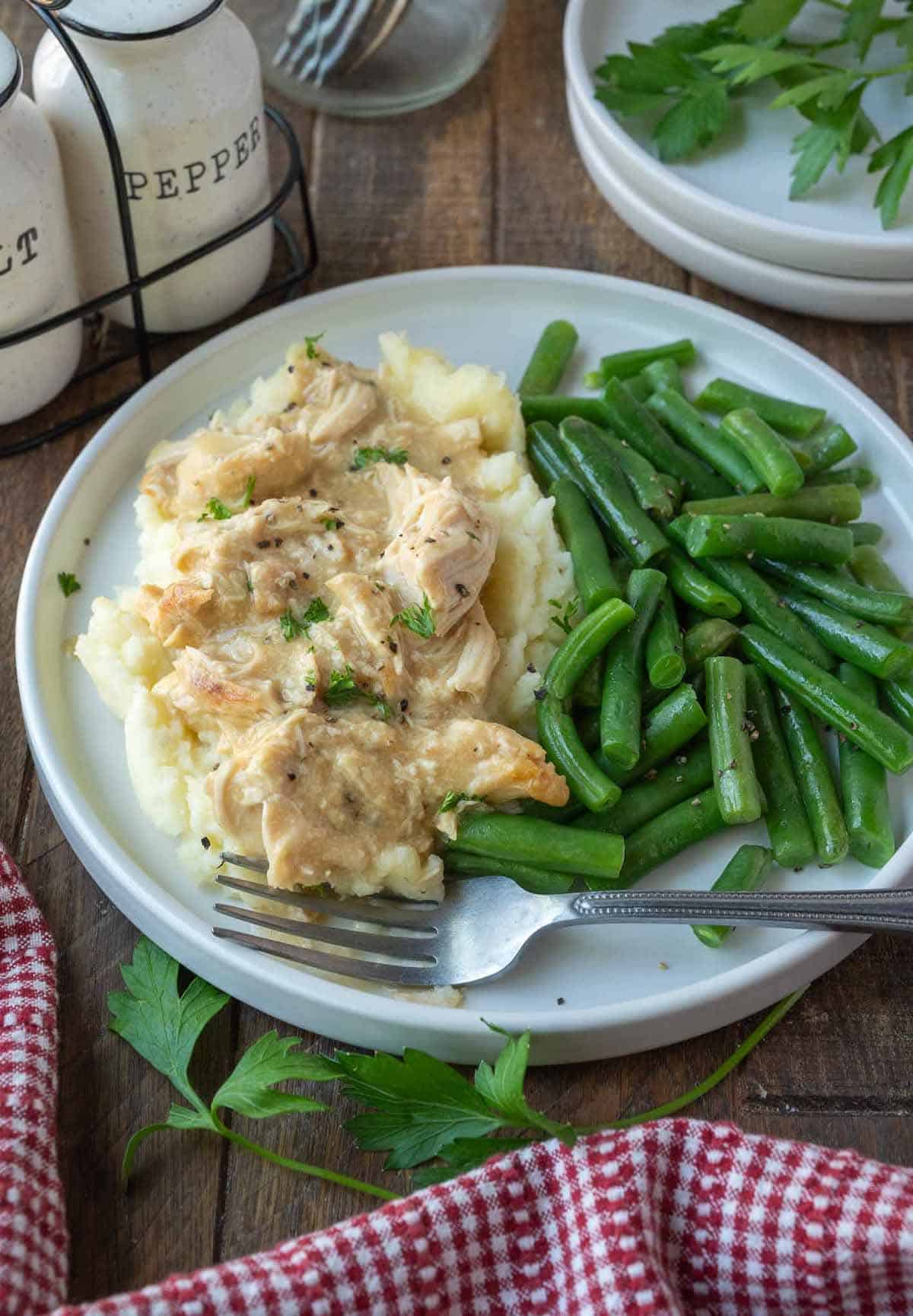 Shredded chicken and gravy on top of mashed potatoes with green beans.