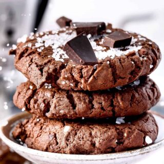 Three chocolate cookies stacked on top of each other with seal salt and chocolate chunks on top.