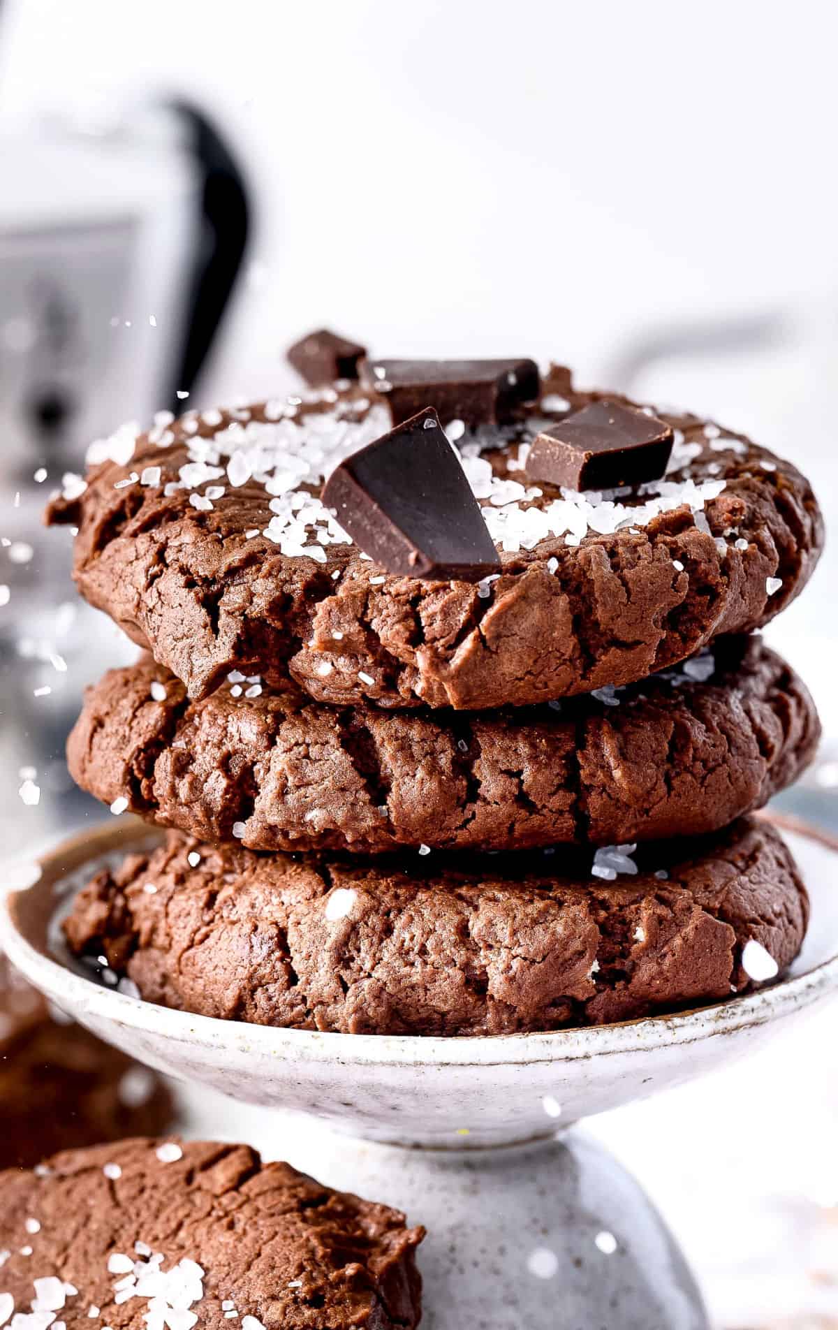 Three chocolate cookies stacked on top of each other with seal salt and chocolate chunks on top.