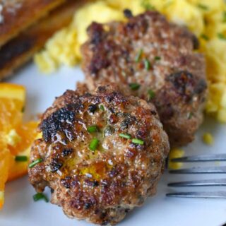 Sausage patties on a plate with eggs and oranges.