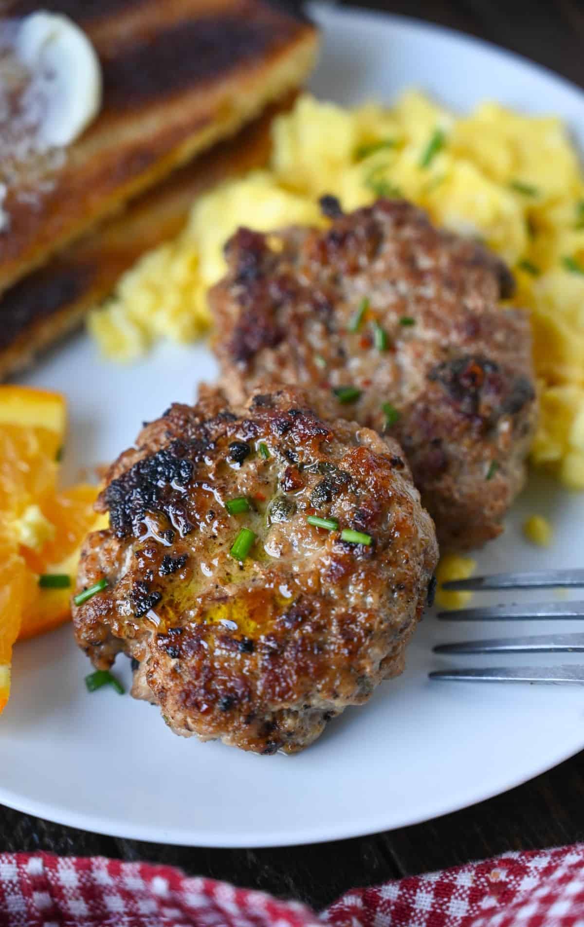 Sausage patties on a plate with eggs and oranges.