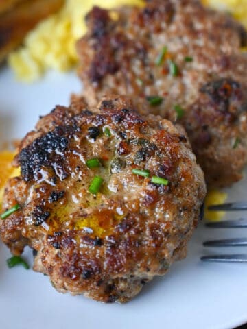 Sausage patties on a plate with eggs and oranges.