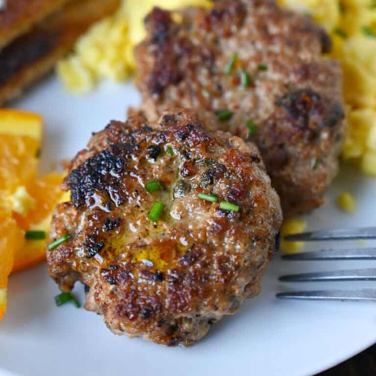 Sausage patties on a plate with eggs and oranges.