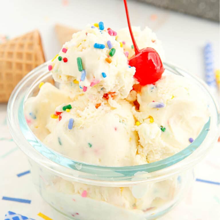 A bowl of birthday cake ice cream with a cherry on top.