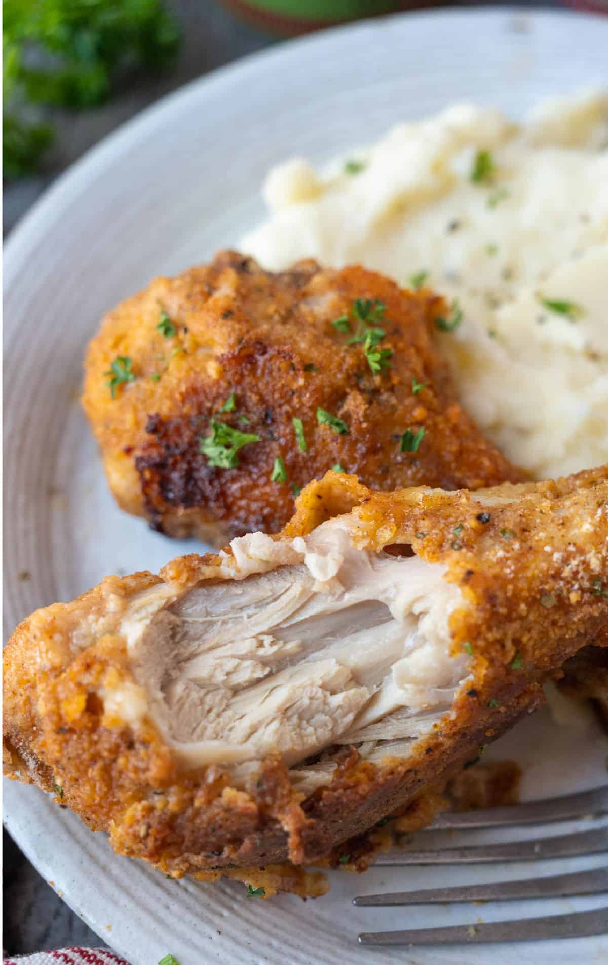 A bite out of a chicken leg placed on a plate with a side of mashed potatoes.
