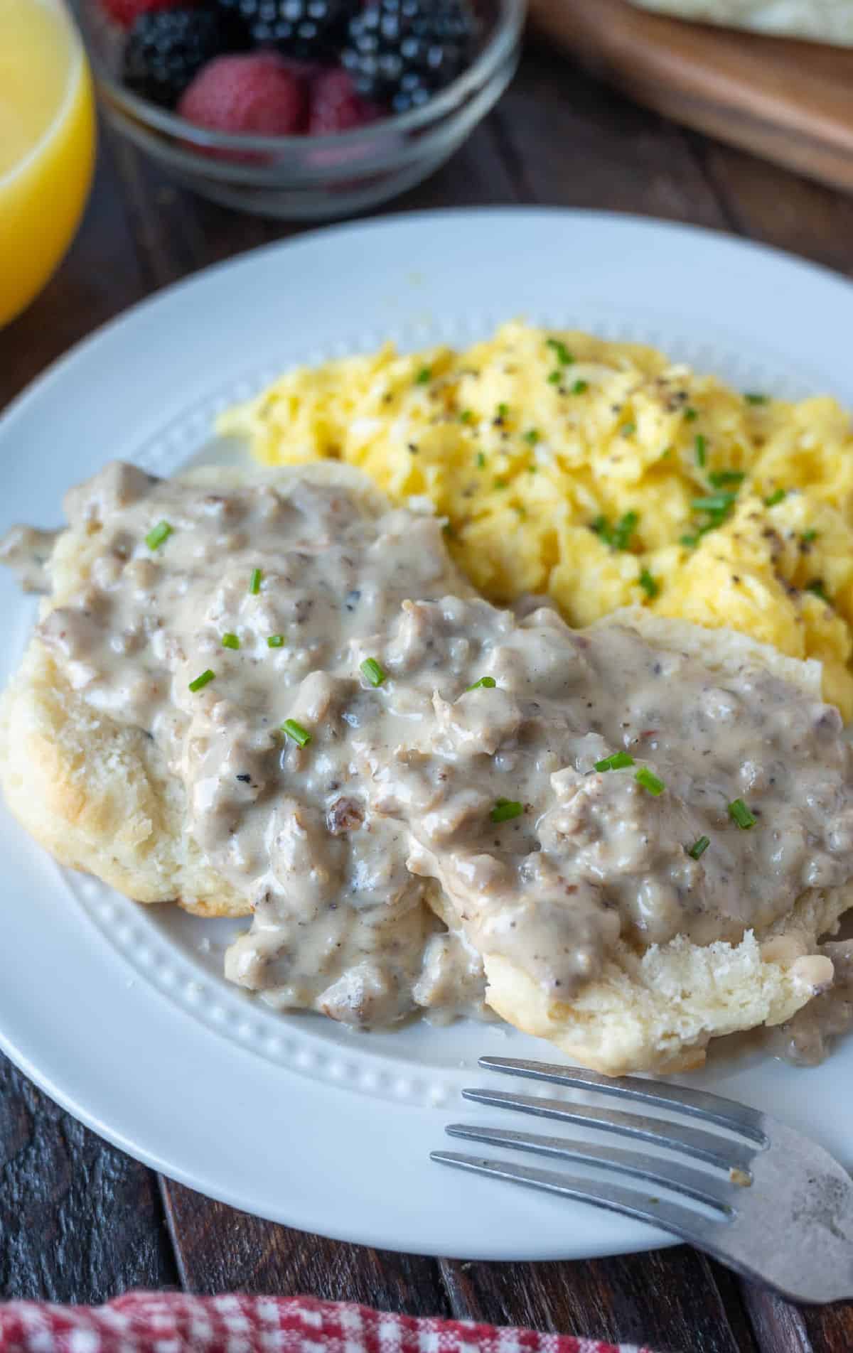 Sausage gravy on top of a biscuit with a side of scrambled eggs.