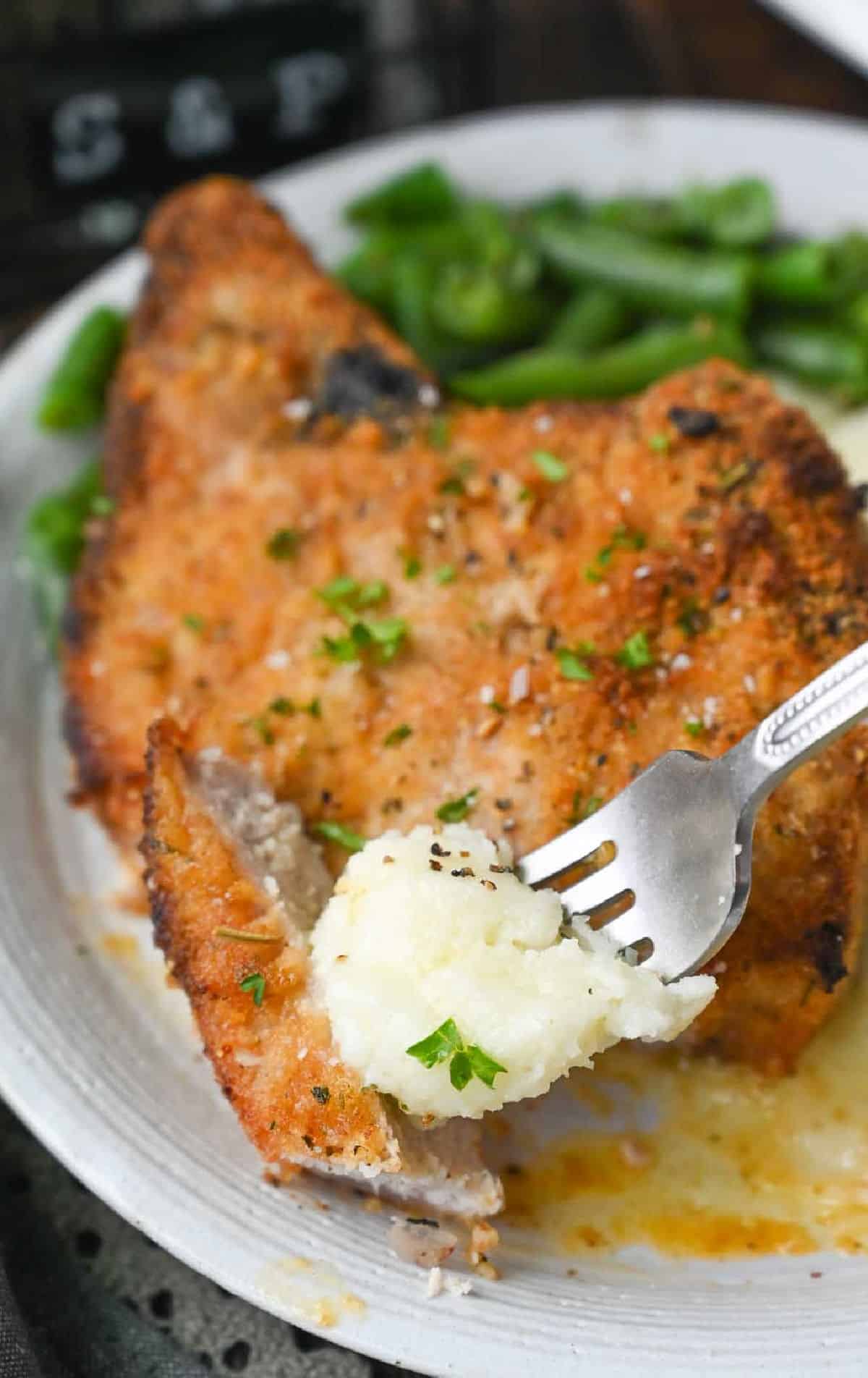 shake and bake pork chop bite with a fork in it and a scoop of mashed potatoes.