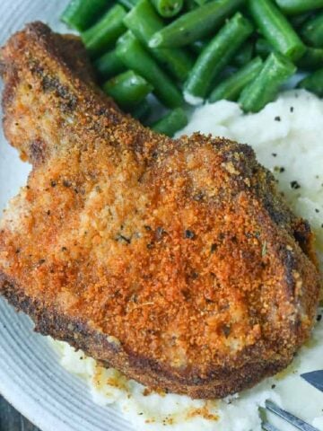 Oven fried pork chop on top of mashed potatoes.