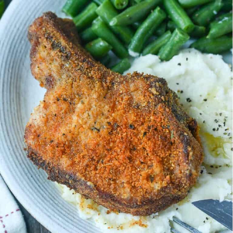 Oven fried pork chop on top of mashed potatoes.